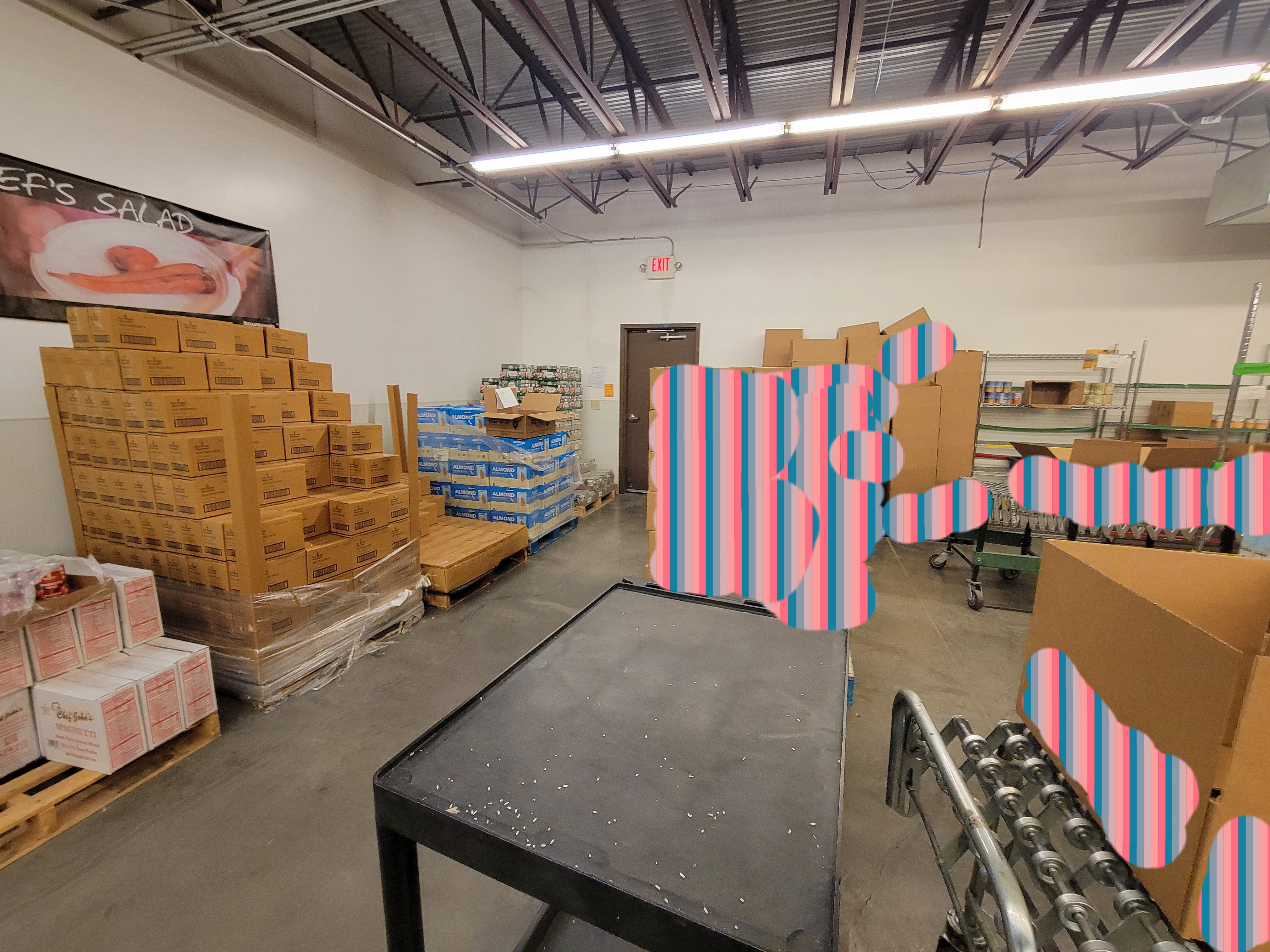 Pallets of food, boxes, conveyor belts, and shelves in a little work station.